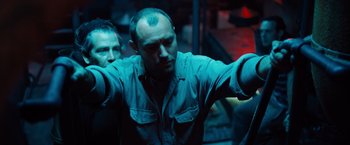 Movie still from “Black Sea” (2014), directed by Kevin Macdonald – Two men are standing in a dark room; Medium shot, Low angle