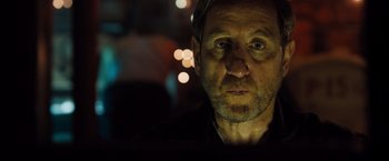 Movie still from “Black Sea” (2014), directed by Kevin Macdonald – A person wearing a black shirt with lights in the background; Close Up shot, Over the shoulder angle