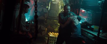 Movie still from “Black Sea” (2014), directed by Kevin Macdonald – A man holding another man in a room with lights; Medium shot, Over the shoulder angle