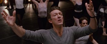 Movie still from “Black Swan” (2010), directed by Darren Aronofsky – A man in a grey sweater is doing a yoga pose; Close Up shot, Low angle
