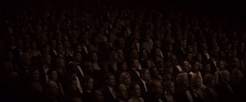 Movie still from “Black Swan” (2010), directed by Darren Aronofsky – A large group of people sitting in a room; Extreme Wide shot, High angle