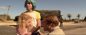 Movie still from “Black Widow” (2021), directed by Cate Shortland – A man and two girls sitting next to each other on the beach; Medium shot, Over the shoulder angle