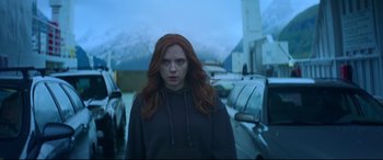 Movie still from “Black Widow” (2021), directed by Cate Shortland – A woman with red hair standing in a parking lot next to cars; Medium shot, Low angle