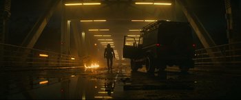 Movie still from “Black Widow” (2021), directed by Cate Shortland – A man walking through a tunnel with a car on fire in front of him; Wide shot, Low angle