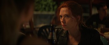 Movie still from “Black Widow” (2021), directed by Cate Shortland – A person sitting at a table with a beer; Close Up shot, Over the shoulder angle
