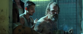 Movie still from “Black Widow” (2021), directed by Cate Shortland – A man with a beard is getting tattooed by another man; Medium shot, Over the shoulder angle