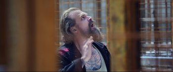 Movie still from “Black Widow” (2021), directed by Cate Shortland – A man with a beard and a tattoo on his face; Medium shot, Low angle