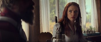 Movie still from “Black Widow” (2021), directed by Cate Shortland – A woman sitting at a table with a coffee pot in front of a window; Close Up shot, Over the shoulder angle