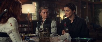 Movie still from “Black Widow” (2021), directed by Cate Shortland – Two women are sitting at a table with drinks in front of them; Medium shot, Over the shoulder angle