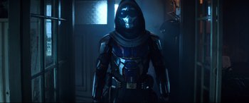 Movie still from “Black Widow” (2021), directed by Cate Shortland – A man in a costume standing in a dark room; Medium shot, Over the shoulder angle