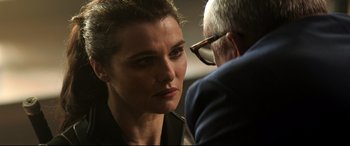 Movie still from “Black Widow” (2021), directed by Cate Shortland – A person wearing glasses and a suit; Close Up shot, Over the shoulder angle