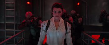 Movie still from “Black Widow” (2021), directed by Cate Shortland – A woman in a white jacket standing in a room; Medium shot, Over the shoulder angle