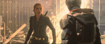 Movie still from “Black Widow” (2021), directed by Cate Shortland – A woman holding a sword in front of a fire; Medium shot, Over the shoulder angle