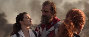 Movie still from “Black Widow” (2021), directed by Cate Shortland – A man with a long beard standing next to a woman; Close Up shot, Over the shoulder angle
