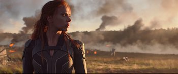 Movie still from “Black Widow” (2021), directed by Cate Shortland – A person in a field with smoke in the background; Medium shot, Low angle