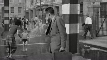 Movie still from “Blackboard Jungle” (1955), directed by Richard Brooks – A black and white photo of a man in a suit holding a briefcase; Wide shot, High angle