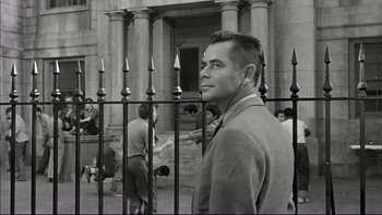 Movie still from “Blackboard Jungle” (1955), directed by Richard Brooks – A black and white photo of a man behind a fence; Medium shot, Over the shoulder angle