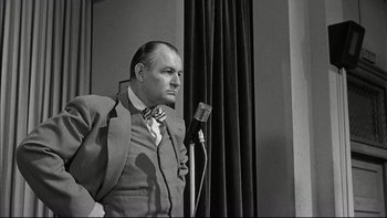 Movie still from “Blackboard Jungle” (1955), directed by Richard Brooks – An old photo of a man in a suit and a microphone; Medium shot, Low angle