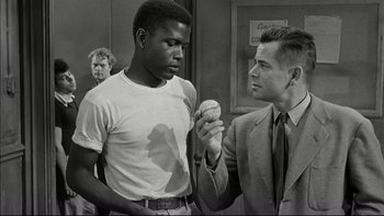 Movie still from “Blackboard Jungle” (1955), directed by Richard Brooks – A man holding a baseball in his hand while another man stands next to him; Medium shot, Over the shoulder angle