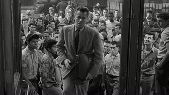 Movie still from “Blackboard Jungle” (1955), directed by Richard Brooks – A man in a suit and tie standing in front of a group of men; Medium shot, High angle