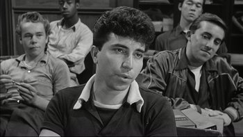 Movie still from “Blackboard Jungle” (1955), directed by Richard Brooks – Black and white photograph of a young man in front of a group of other men; Close Up shot, Over the shoulder angle