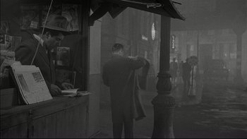 Movie still from “Blackboard Jungle” (1955), directed by Richard Brooks – A man standing in front of a store holding a jacket; Wide shot, High angle