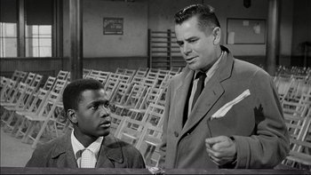 Movie still from “Blackboard Jungle” (1955), directed by Richard Brooks – A man and a man in a suit and tie talking to each other; Medium shot, Low angle