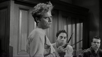 Movie still from “Blackboard Jungle” (1955), directed by Richard Brooks – A man holding a pair of scissors next to another man in a room; Medium shot, Low angle