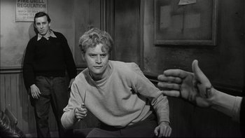 Movie still from “Blackboard Jungle” (1955), directed by Richard Brooks – A man sitting on a chair holding a pair of scissors; Medium shot, Over the shoulder angle