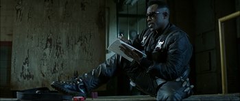 Movie still from “Blade” (1998), directed by Stephen Norrington – A man sitting on the ground writing on a piece of paper; Medium shot, Low angle