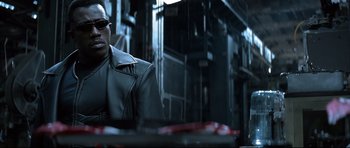 Movie still from “Blade” (1998), directed by Stephen Norrington – A man sitting at a table in front of a building; Close Up shot, Low angle