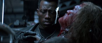 Movie still from “Blade” (1998), directed by Stephen Norrington – A man looking down at his cell phone while holding a knife; Close Up shot, Over the shoulder angle