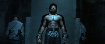 Movie still from “Blade” (1998), directed by Stephen Norrington – A muscular man with no shirt is standing in a dark room; Medium shot, Low angle