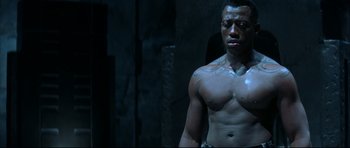 Movie still from “Blade” (1998), directed by Stephen Norrington – A shirtless man standing next to a stone wall; Close Up shot, High angle