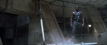 Movie still from “Blade” (1998), directed by Stephen Norrington – A man standing next to a sword in a room; Wide shot, Low angle