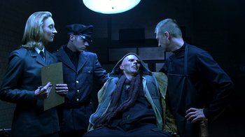 Movie still from “Blade II” (2002), directed by Guillermo del Toro – A man sitting in a chair next to two other men; Medium shot, Low angle