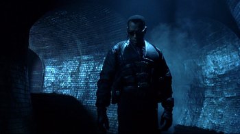 Movie still from “Blade II” (2002), directed by Guillermo del Toro – A man standing in the dark in front of a brick wall; Medium shot, Low angle