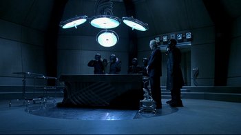 Movie still from “Blade II” (2002), directed by Guillermo del Toro – A group of people standing around a table in a dark room; Wide shot, High angle