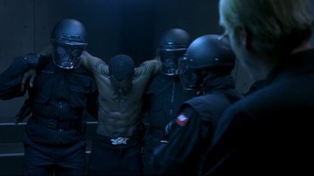 Movie still from “Blade II” (2002), directed by Guillermo del Toro – A group of police officers standing next to a man with his hands on his chest; Medium shot, Over the shoulder angle