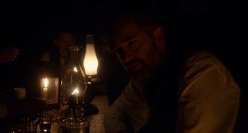 Movie still from “Tesla” (2020), directed by Michael Almereyda – A man sitting in front of an oil lamp in a dimly - lit room; Close Up shot, Over the shoulder angle