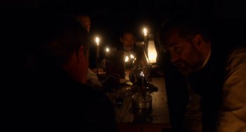 Movie still from “Tesla” (2020), directed by Michael Almereyda – A group of people sitting around a table with candles; Medium shot, Over the shoulder angle