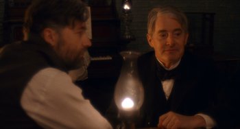 Movie still from “Tesla” (2020), directed by Michael Almereyda – Two men sitting at a table with an oil lamp in front of them; Medium shot, Over the shoulder angle