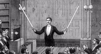 Movie still from “Tesla” (2020), directed by Michael Almereyda – An illustration of a man holding two mallets in front of an orchestra; Medium shot, Over the shoulder angle