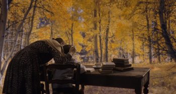 Movie still from “Tesla” (2020), directed by Michael Almereyda – A woman sitting at a table in front of a tree; Wide shot, High angle