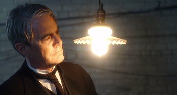 Movie still from “Tesla” (2020), directed by Michael Almereyda – A man standing under a hanging light in the dark; Close Up shot, Low angle