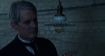 Movie still from “Tesla” (2020), directed by Michael Almereyda – A man standing under a hanging light in a room; Close Up shot, Low angle