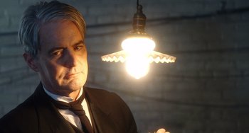 Movie still from “Tesla” (2020), directed by Michael Almereyda – A man in a suit and tie standing next to a light; Close Up shot, Low angle