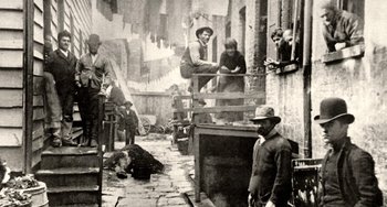 Movie still from “Tesla” (2020), directed by Michael Almereyda – A group of men standing on the side of a building; Wide shot, High angle