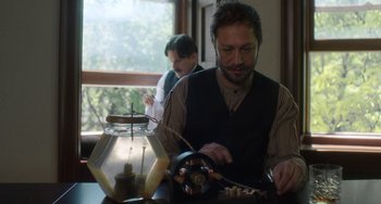 Movie still from “Tesla” (2020), directed by Michael Almereyda – A man sitting in front of a table with a jar; Medium shot, Low angle