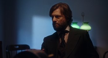 Movie still from “Tesla” (2020), directed by Michael Almereyda – A man in a suit and tie looking at a book; Close Up shot, Over the shoulder angle